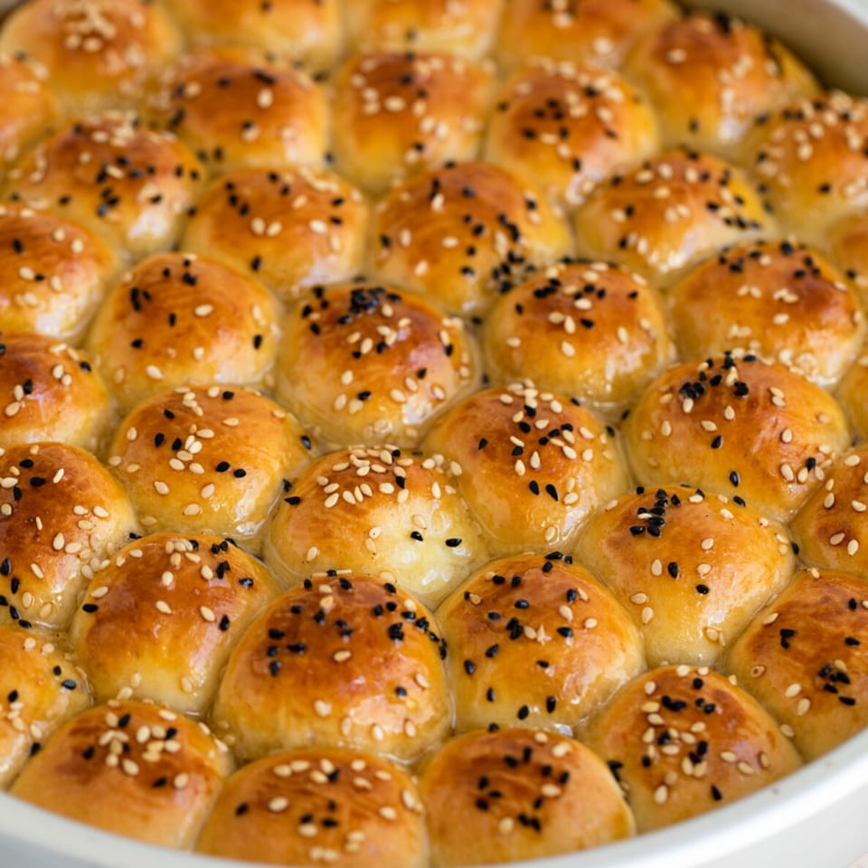 Golden brown baked goods, possibly sticky buns or rolls, topped with white and black sesame seeds.
