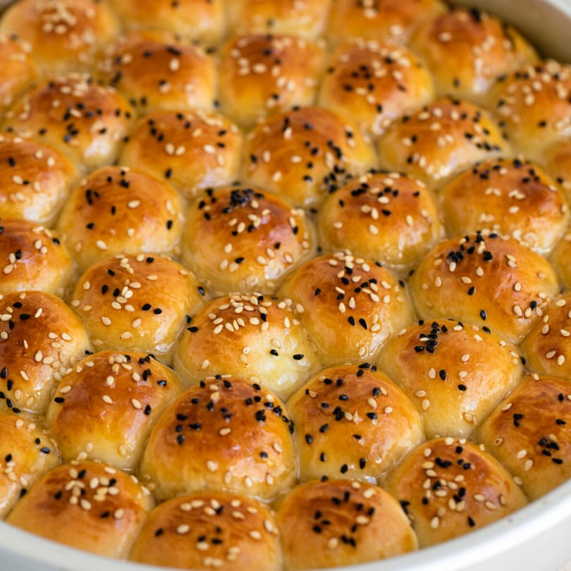Golden brown baked goods, possibly sticky buns or rolls, topped with white and black sesame seeds.