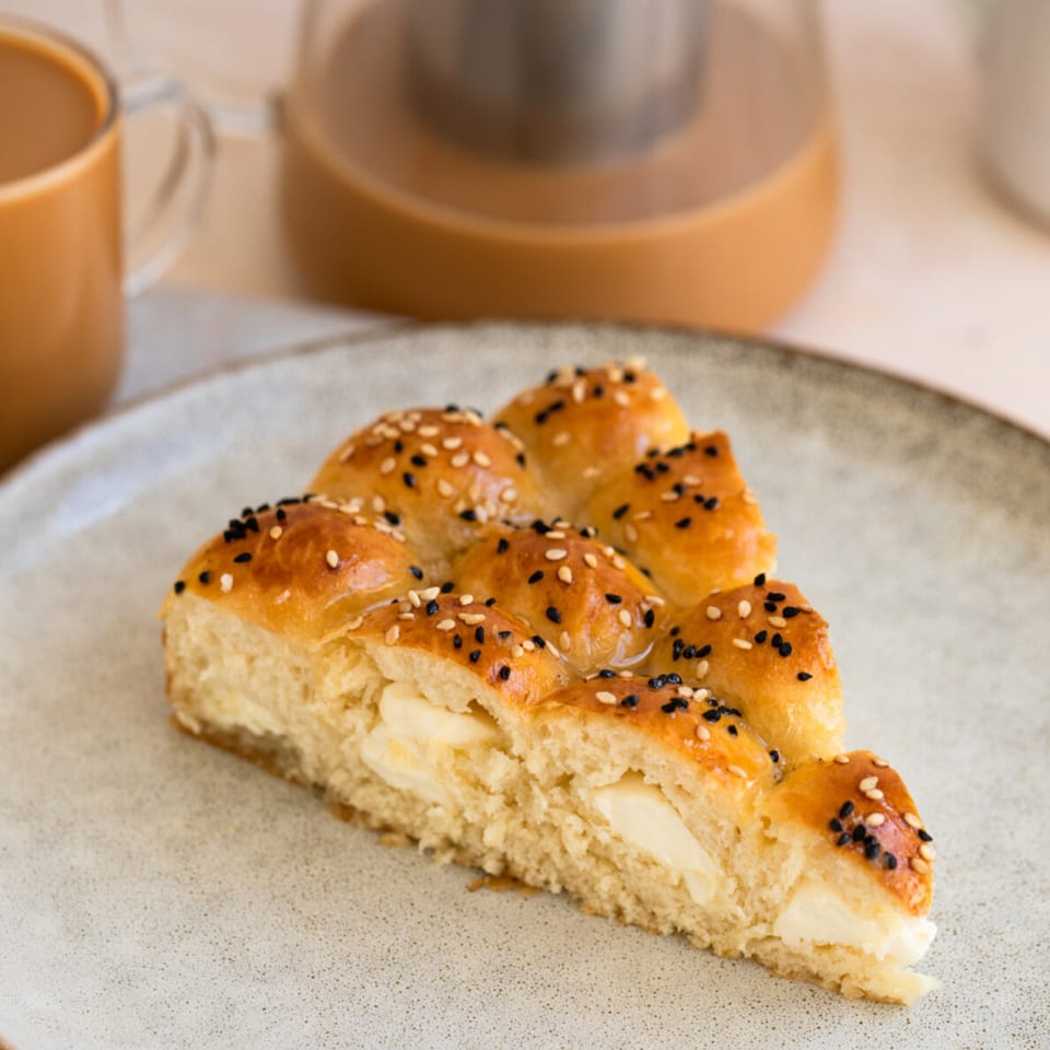 A slice of golden-brown pastry with white and black sesame seeds, filled with cream cheese.